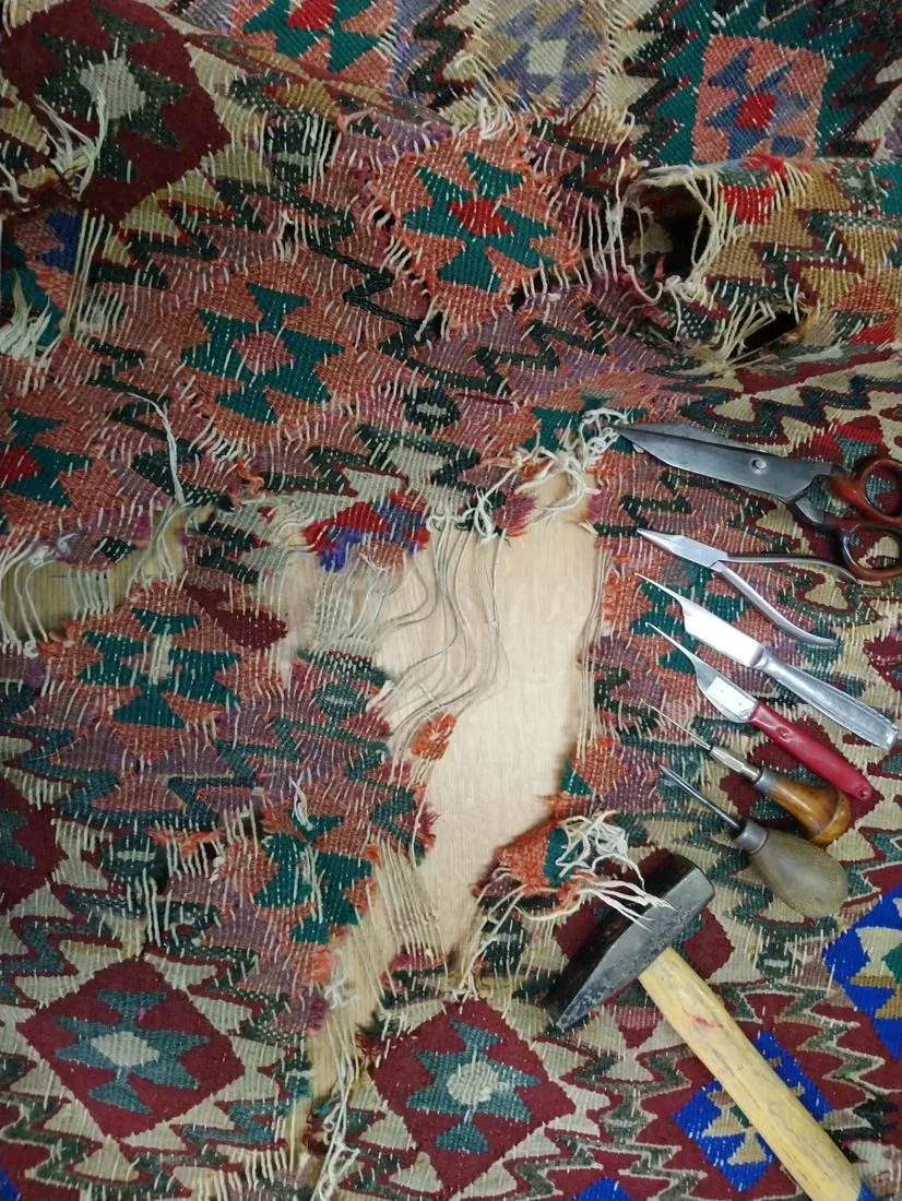 Mottenschaden an einem Kelim vor der Restauration, mit Werkzeug im Atelier